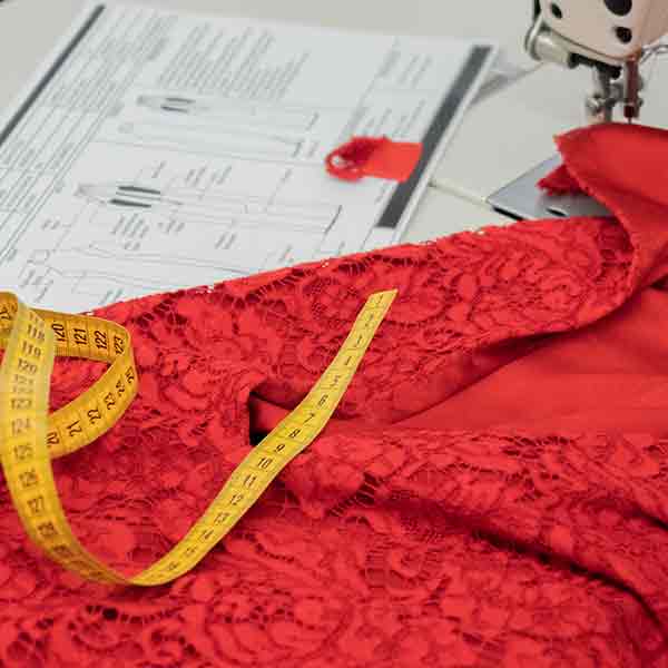 A red flower dress being measured with a tech pack for assistance on top of a sewing machine